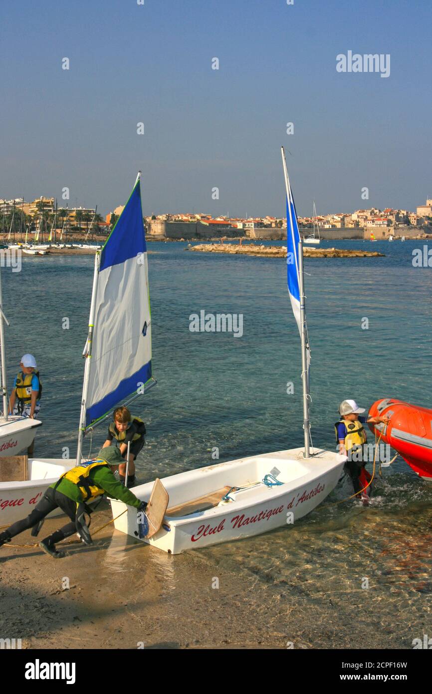 Scuola di marinai per bambini, piccola barca a vela. Studenti con piccole barche a vela in Plage du Ponteil Bay. Il capretto duro mette la barca a vela sull'acqua. Foto Stock