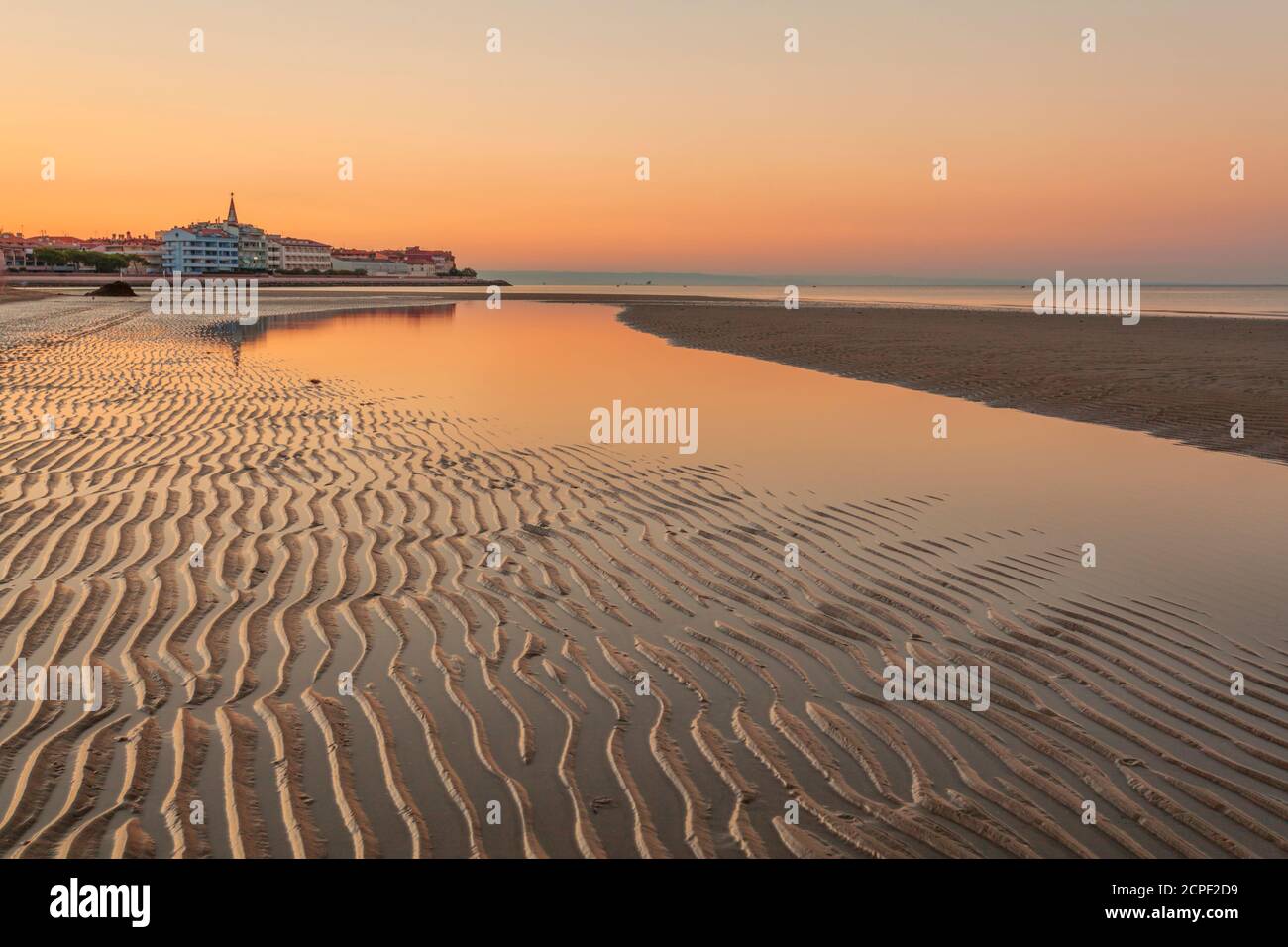 Colorata spiaggia arancione al tramonto con motivi di sabbia ondulata la marea in corso e le riflessioni sull'acqua del laguna in una tranquilla panoramica Foto Stock