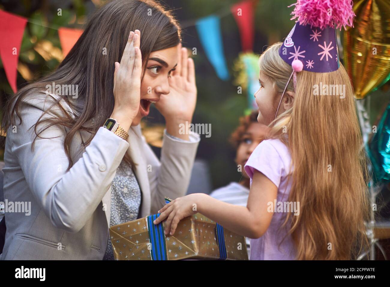 bella bruna caucasica giocare peek un boo con carino poco bionda ragazza a festa di compleanno Foto Stock