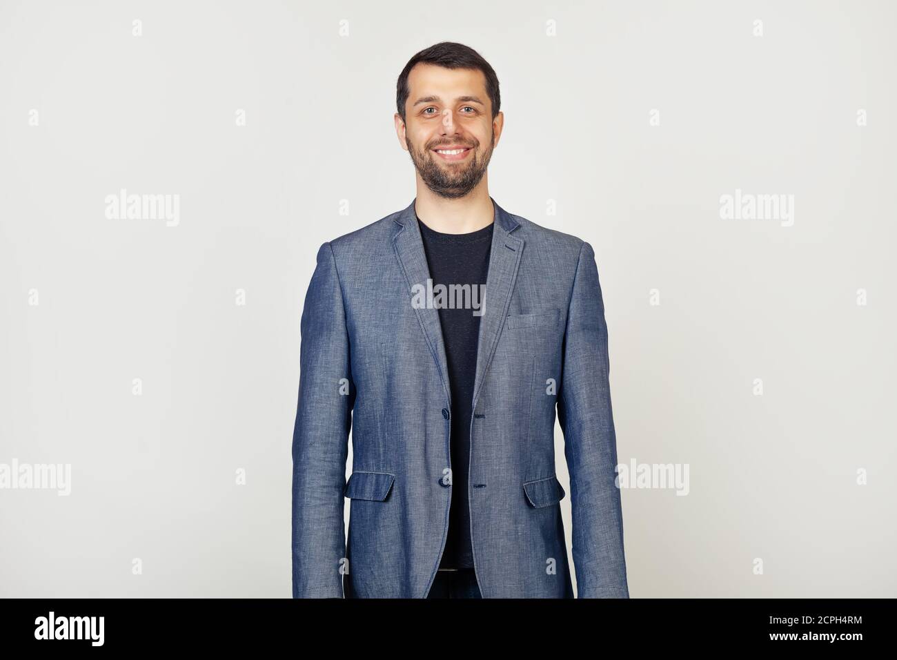 Giovane uomo d'affari con un sorriso, un uomo con una barba in una giacca, con un sorriso felice e fresco sul viso. Persona fortunata. Ritratto di un uomo su sfondo grigio. Foto Stock