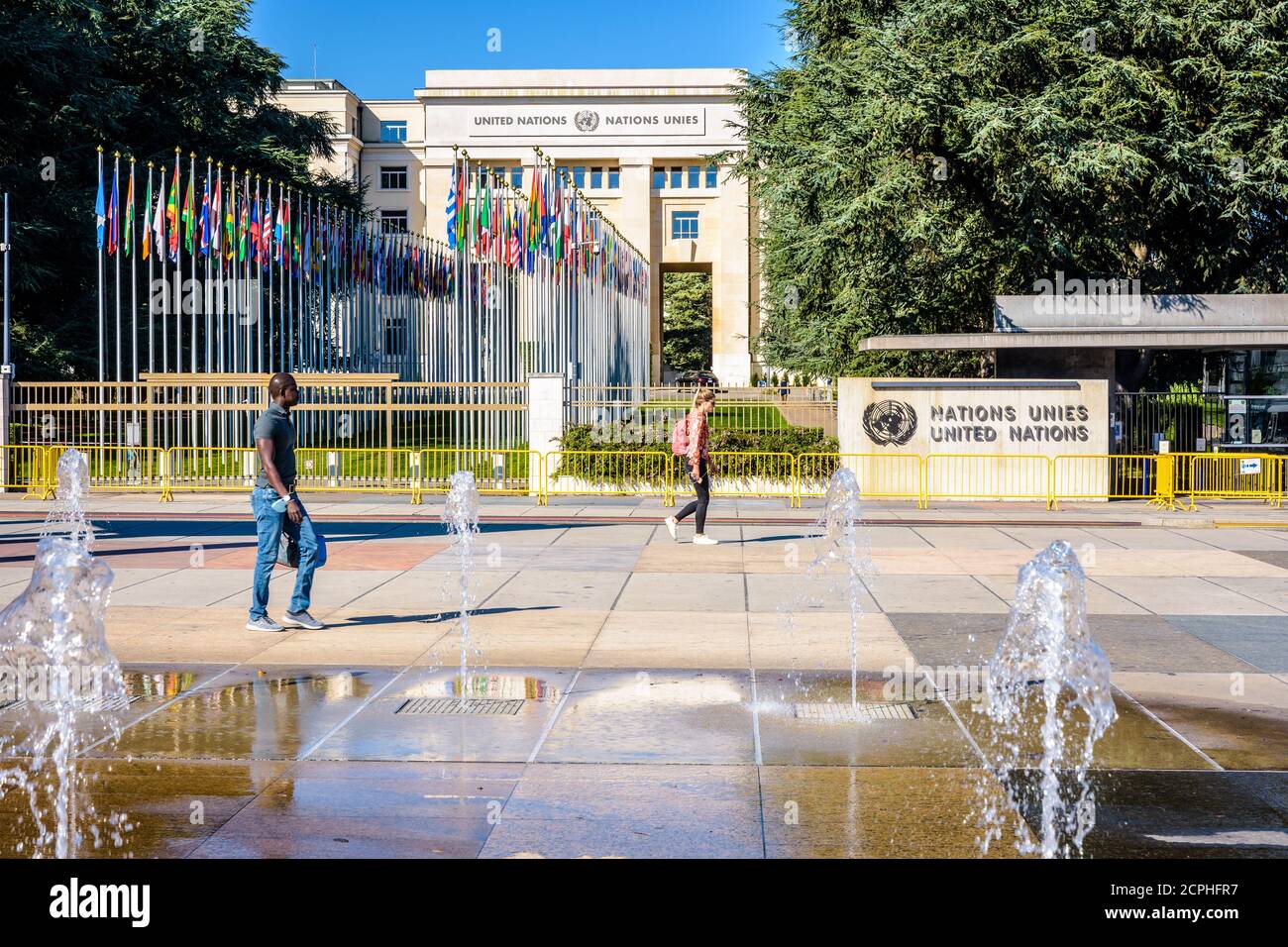 Persone che camminano all'ingresso del Palazzo delle Nazioni, sede dell'Ufficio delle Nazioni Unite a Ginevra, Svizzera, e il viale delle bandiere. Foto Stock