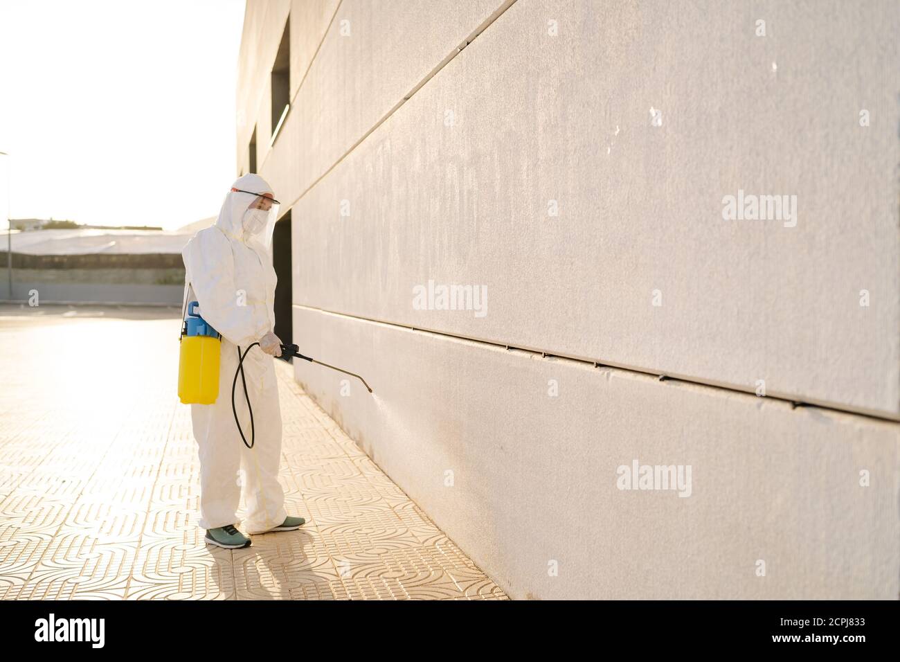 Uomo in tuta anti-virus e maschera disinfettante edifici con lo spruzzatore. Foto Stock