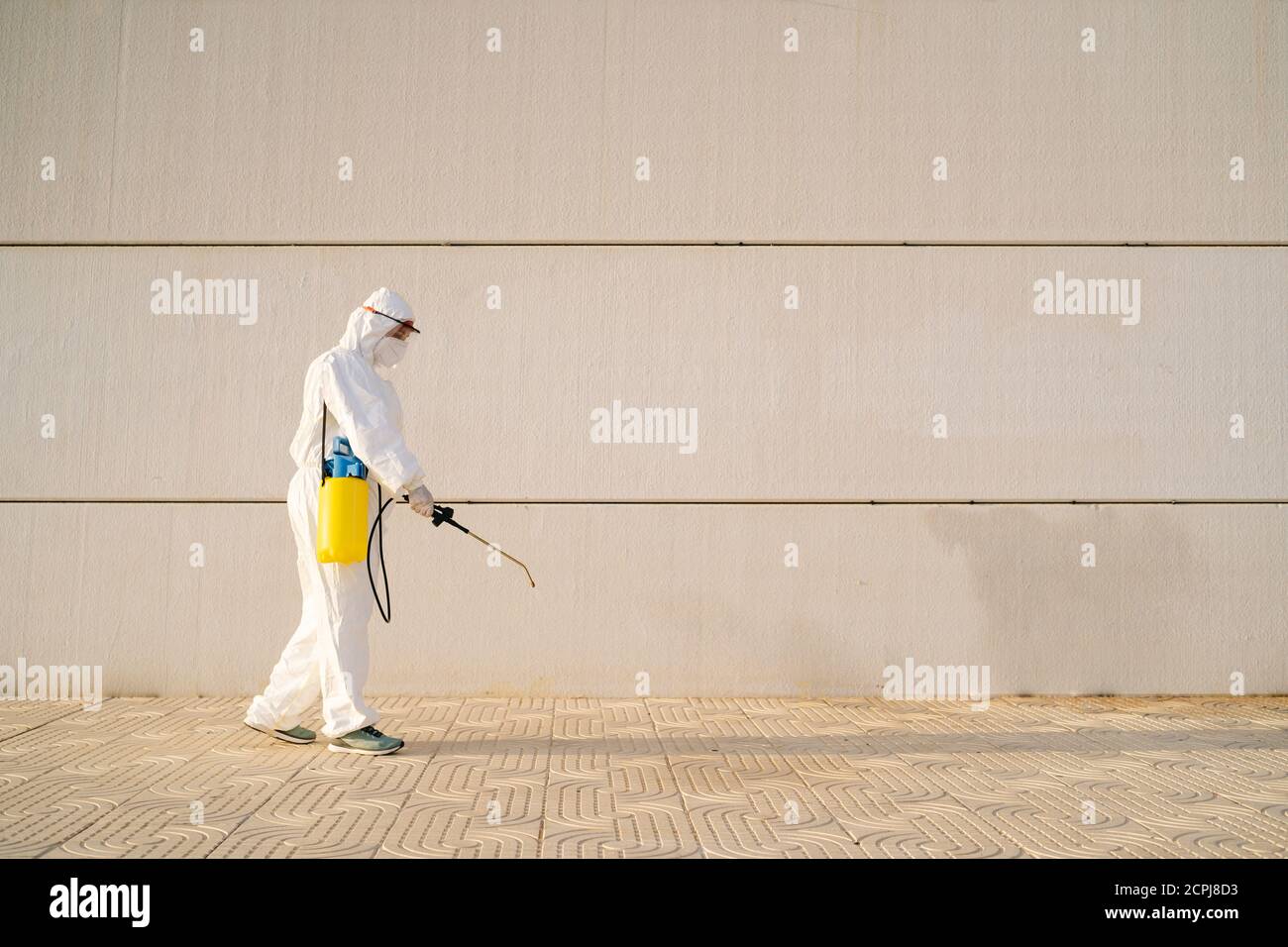 Uomo in tuta anti-virus e maschera disinfettante edifici con lo spruzzatore. Foto Stock