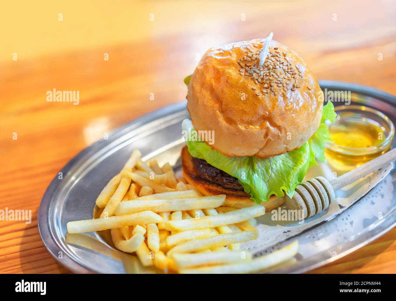 Delizioso hamburger con succulente patatine e lattuga in ciambelle di semi di sesamo con patate fritte e un cucchiaino per la salsa al miele. Foto Stock