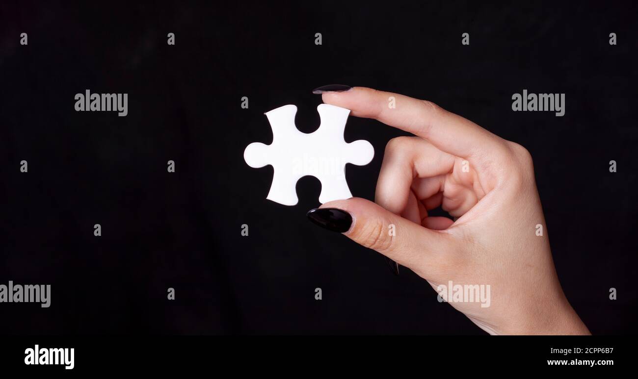 Mano della donna che tiene un elemento di puzzle bianco isolato su sfondo nero. Foto Stock
