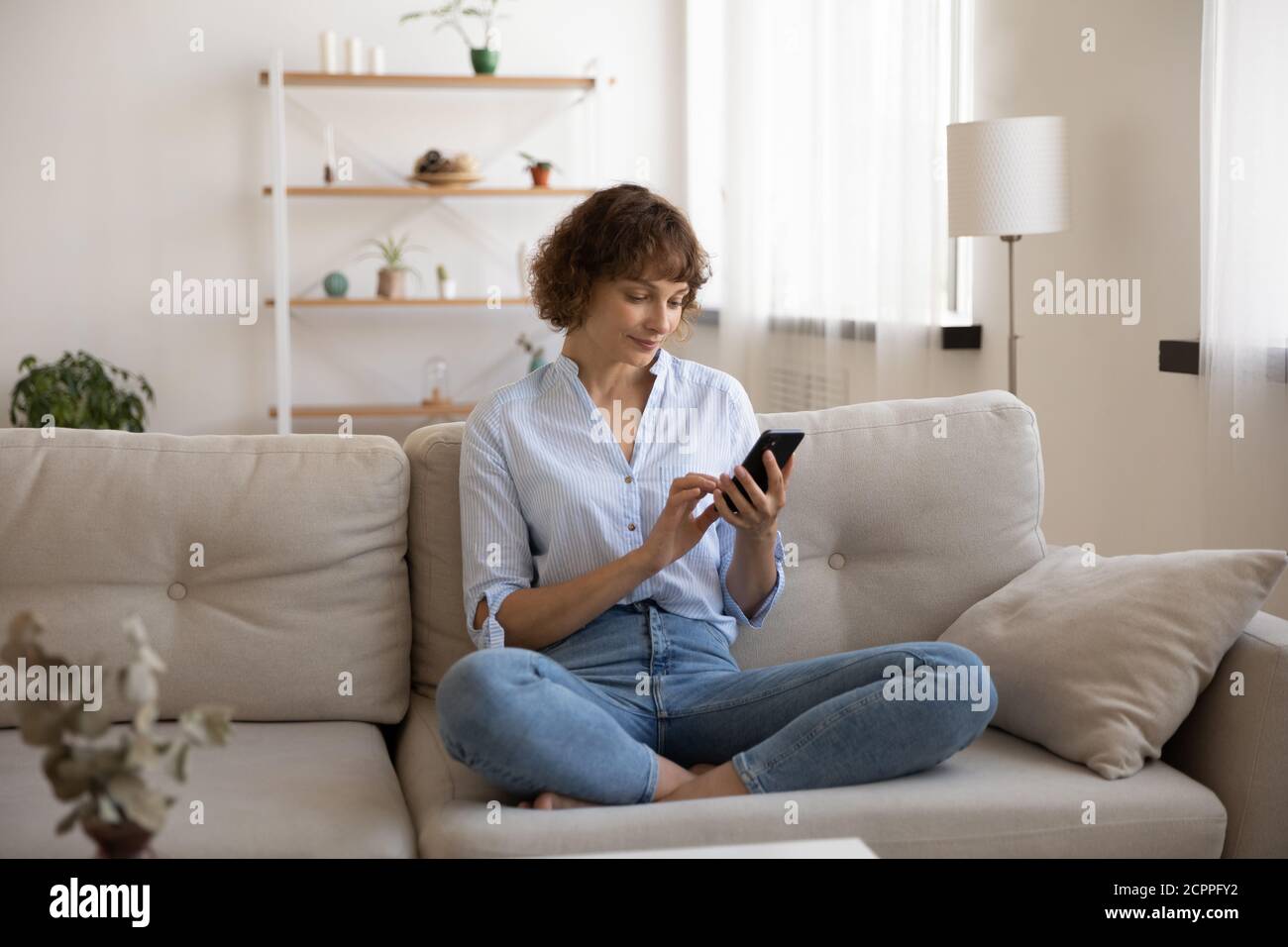 Donna caucasica seduto sul divano utilizzando uno smartphone Foto Stock