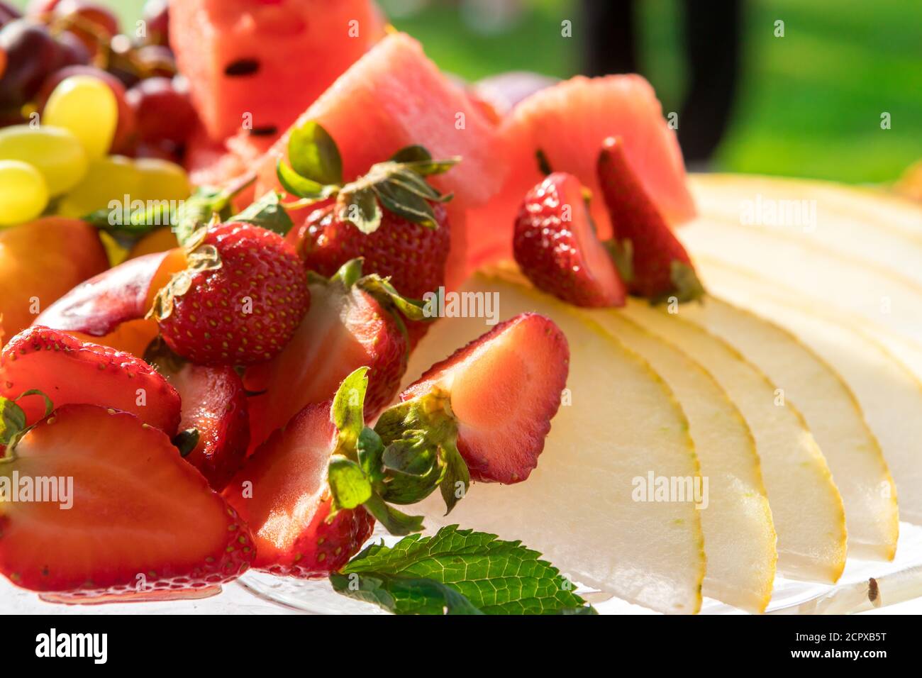 Fragole tagliate a fette, melone, pesche, uva su un piatto primo piano Foto Stock