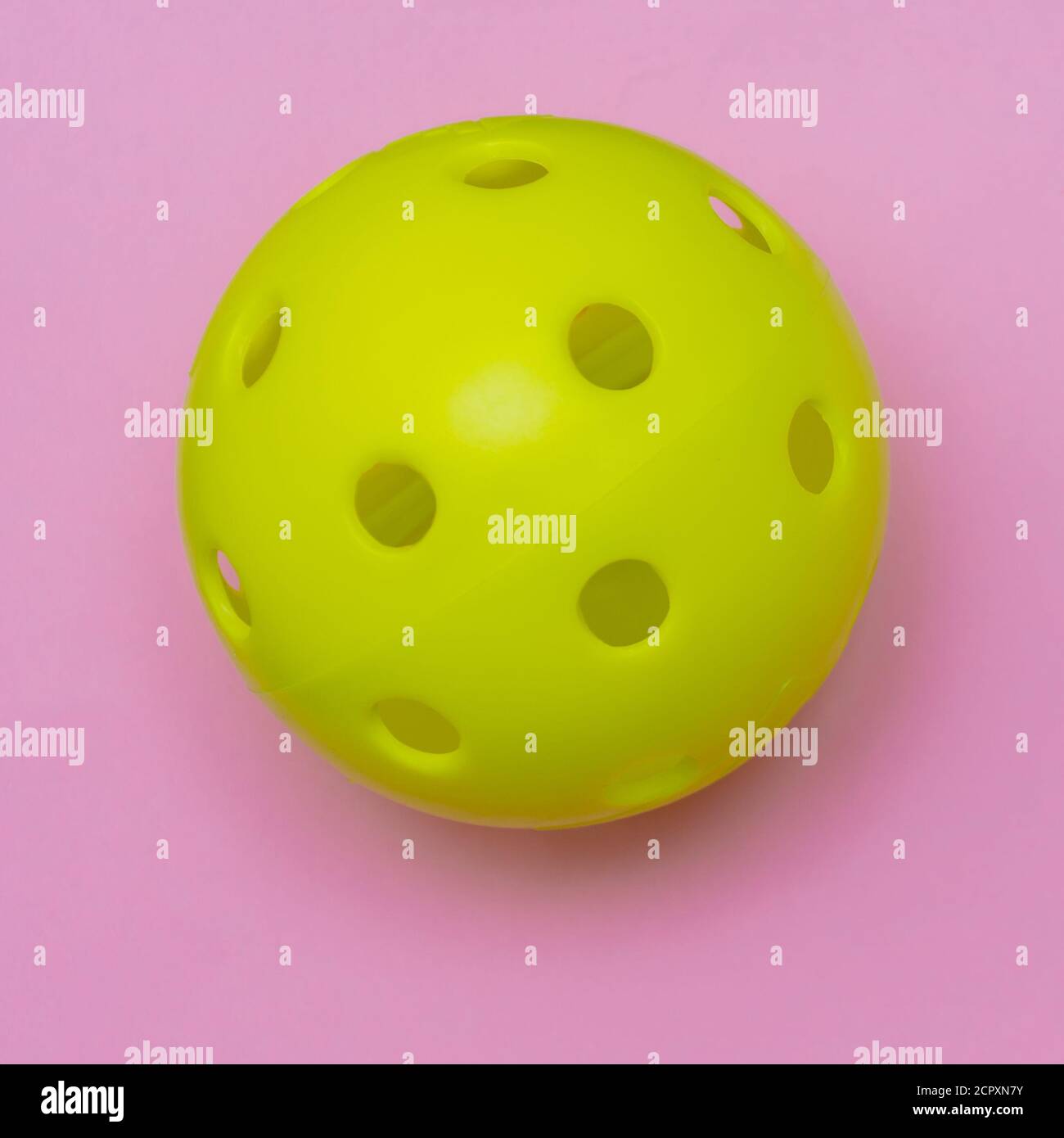 Di colore giallo brillante pickleball o sfera whiffle su un solido rosa luminoso appartamento sfondo laici che simboleggiano sport e attività con copia spazio. Foto Stock