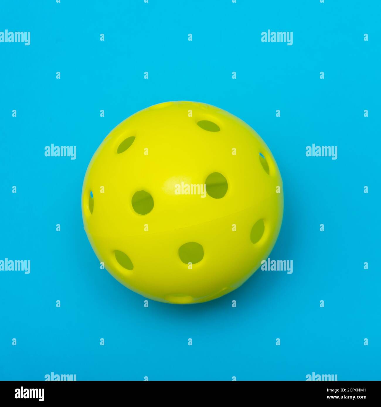 Di colore giallo brillante pickleball o sfera whiffle su un solido aqua blue piatto sfondo laici che simboleggiano sport e attività con copia spazio. Foto Stock