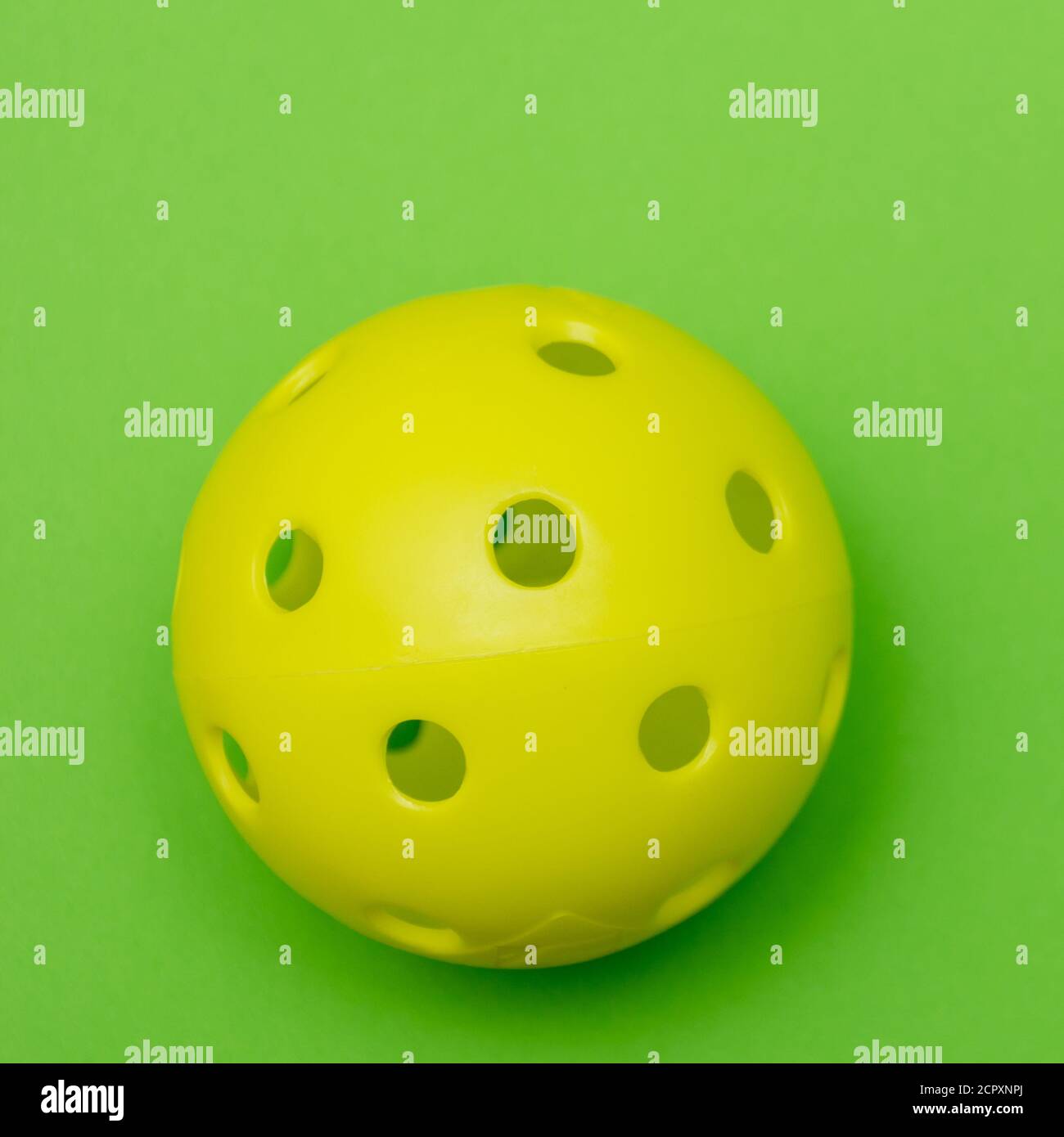 Di colore giallo brillante pickleball o sfera whiffle su un solido verde chiaro piatto sfondo laici che simboleggiano sport e attività con copia spazio. Foto Stock
