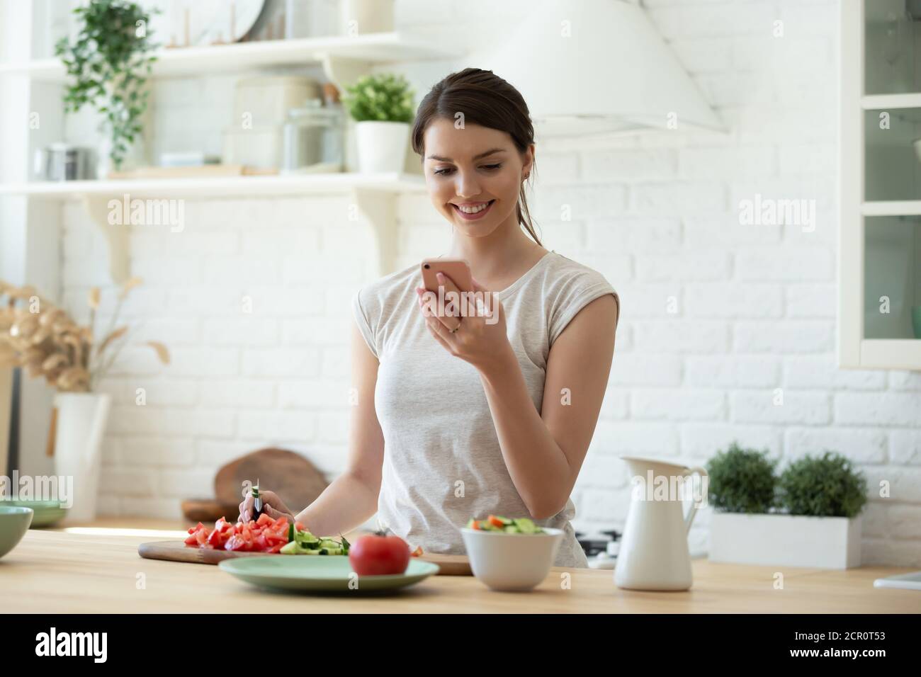 Giovane donna che cucina e che usa il telefono cellulare Foto Stock
