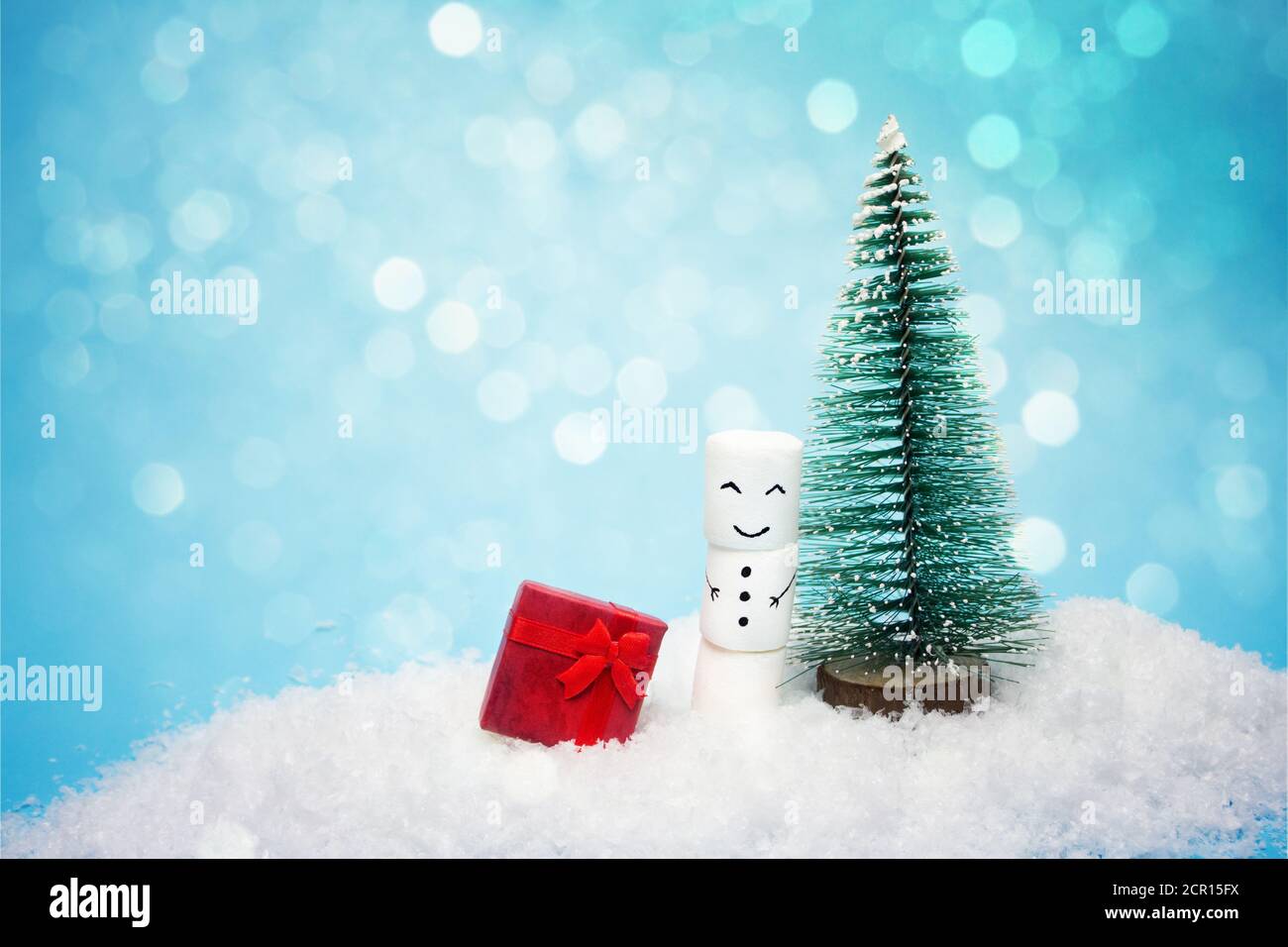 Pupazzo di neve è in piedi vicino a un piccolo yolka nella neve, foto con effetto bokeh di fondo. Scheda di Natale Foto Stock