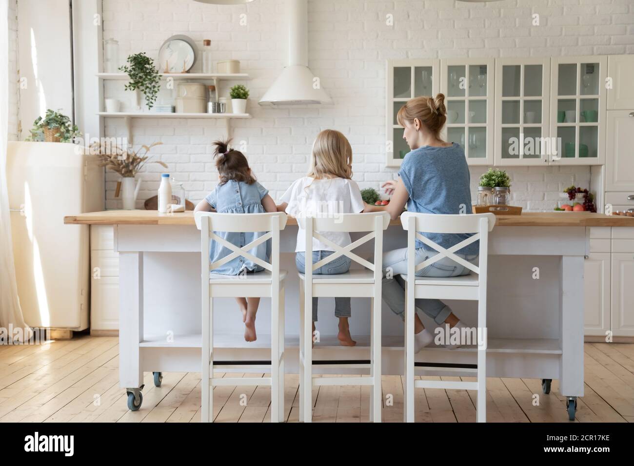 Mamma aiuta le piccole figlie a provare la mano a cucinare Foto Stock