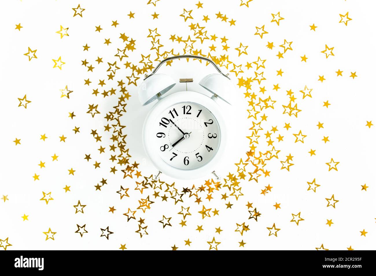 Cornice rotonda, sveglia ricoperta di confetti stelle dorate, decorazione glitter su uno sfondo bianco, festoso. Modello di Natale o Capodanno. Disposizione piatta Foto Stock