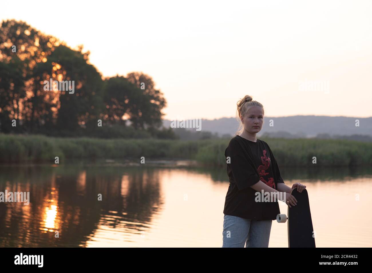 La ragazza si erge sul lago con un longbard al tramonto Foto Stock