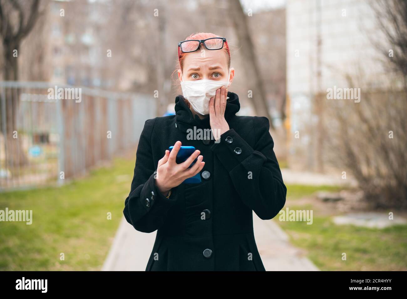 Donna in strada durante l'epidemia di covid-19 guarda la macchina fotografica. Ragazza in maschera spaventato dalle notizie di diffusione del virus. Concetto di panico e paura. Foto Stock
