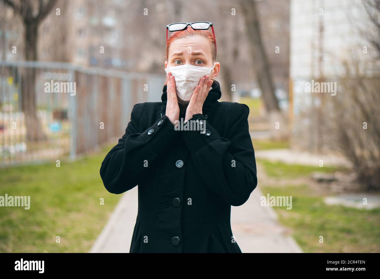 Ragazza in maschera spaventato dalle notizie di diffusione del virus. Donna in strada durante l'epidemia di covid-19 guarda la macchina fotografica. Concetto di panico e paura. Foto Stock