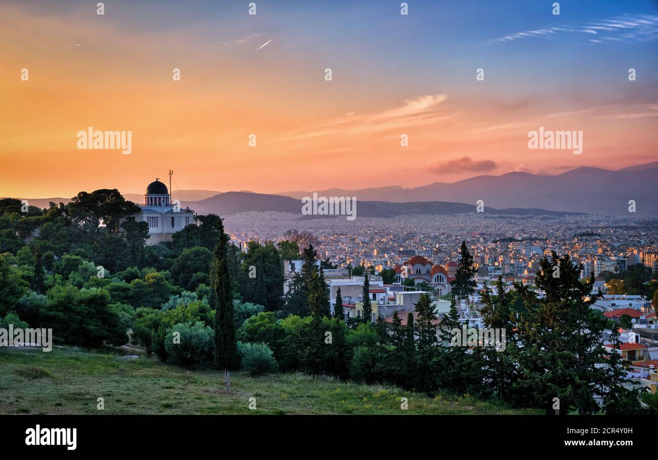 Vista di Atene, Grecia e le zone residenziali dalla collina di Pnyx in luce solare soffusa e il grande cielo del tramonto. Osservatorio nazionale di Atene in primo piano. Foto Stock