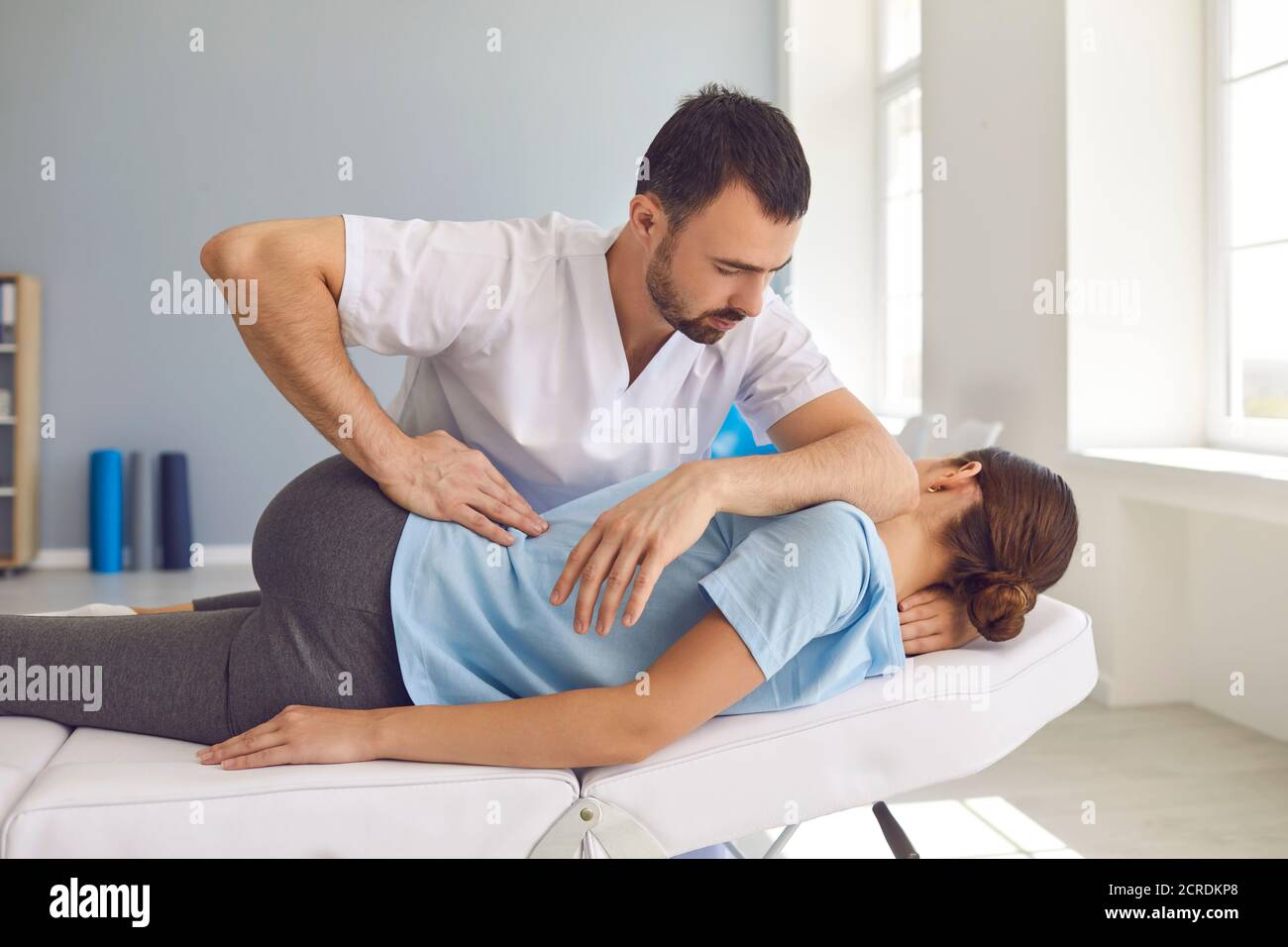 Uomo medico chiropractor o osteopath che fissa le donne sdraiate indietro dentro clinica di terapia manuale Foto Stock