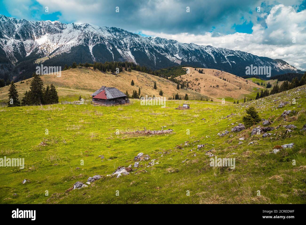 Splendido luogo di campagna alpino con malghe in legno e neve Piatra Craiului montagne sullo sfondo, Pestera villaggio, Transilvania, Romania, e Foto Stock