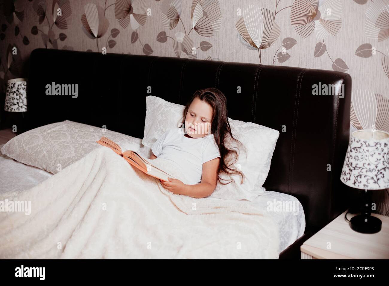 il bambino è seduto sul letto coperto da una coperta chiara e leggere un libro, fiabe prima di andare a letto Foto Stock
