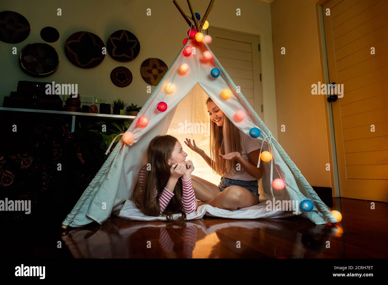 Madre felice e figlia all'interno della tenda tepee in camera da letto, godere di parlare e raccontare la storia; concetto di relazione di famiglia. Foto Stock