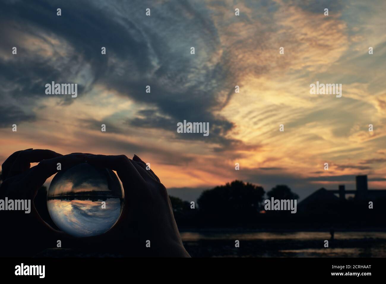 Mani femminili che tengono la lensball davanti ad un cielo bello e drammatico al tramonto Foto Stock