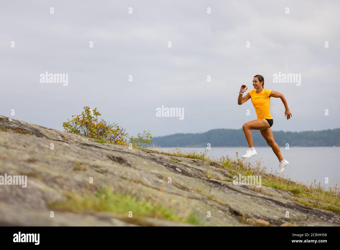 Vista laterale di una donna che fa una corsa ad alta intensità sul fianco della montagna vicino al mare Foto Stock