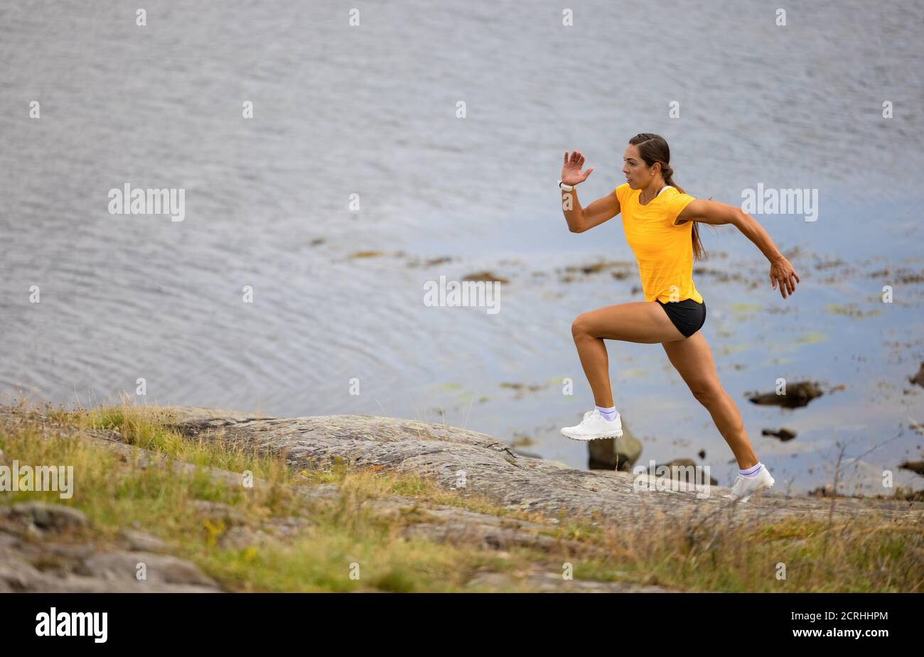 Donna fitness focalizzata che fa correre ad alta intensità sul fianco della montagna mare Foto Stock