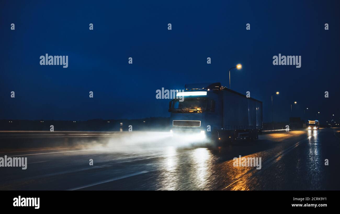 Blue Long Haul semi-Truck con Cargo Trailer Full of Goods viaggia di notte sulla Freeway Road, guidando attraverso il Continente attraverso pioggia, nebbia, neve Foto Stock