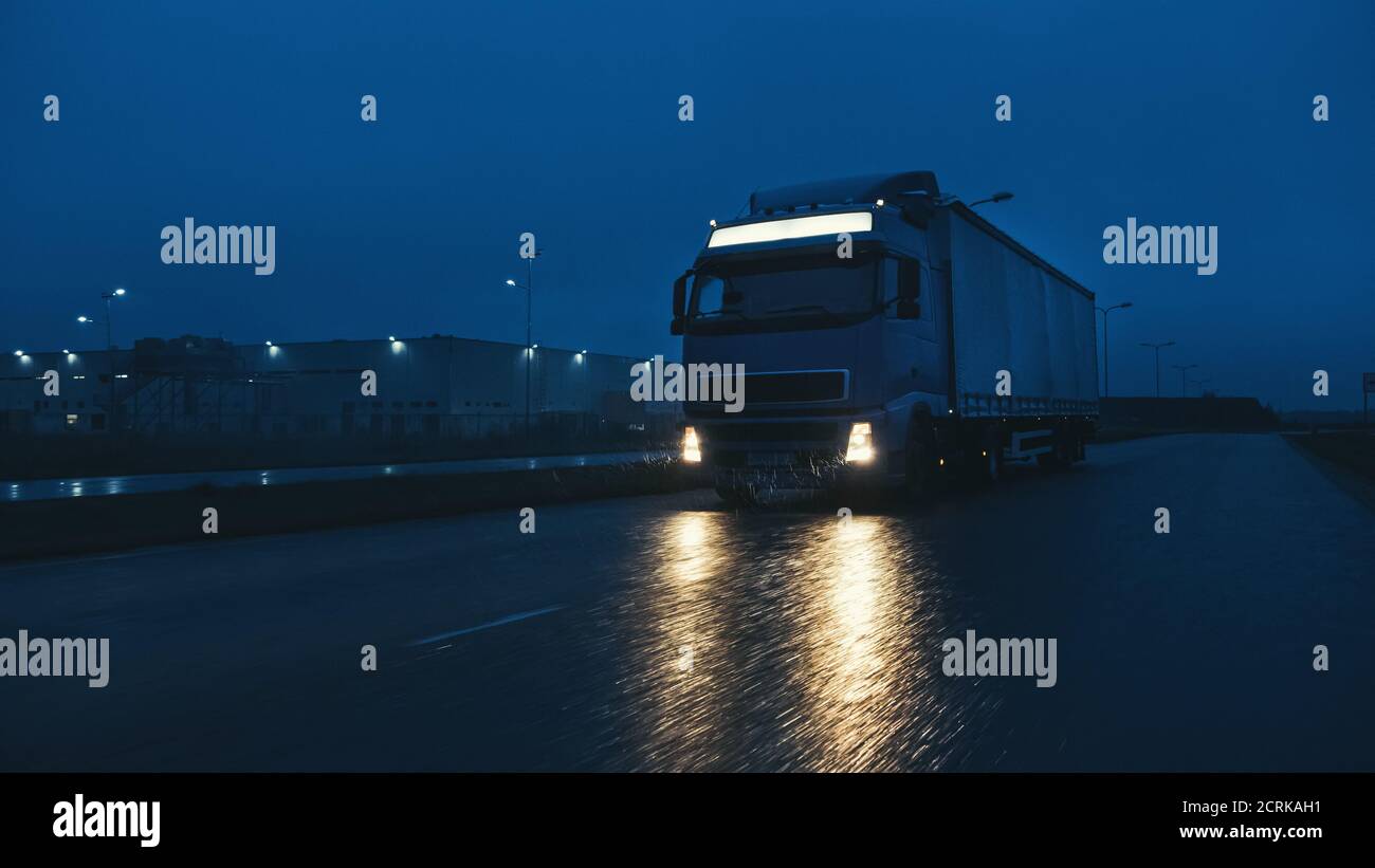 Blue Long Haul semi-Truck con Cargo Trailer Full of Goods viaggia di notte sulla Freeway Road, guidando attraverso il Continente attraverso pioggia, nebbia, neve Foto Stock