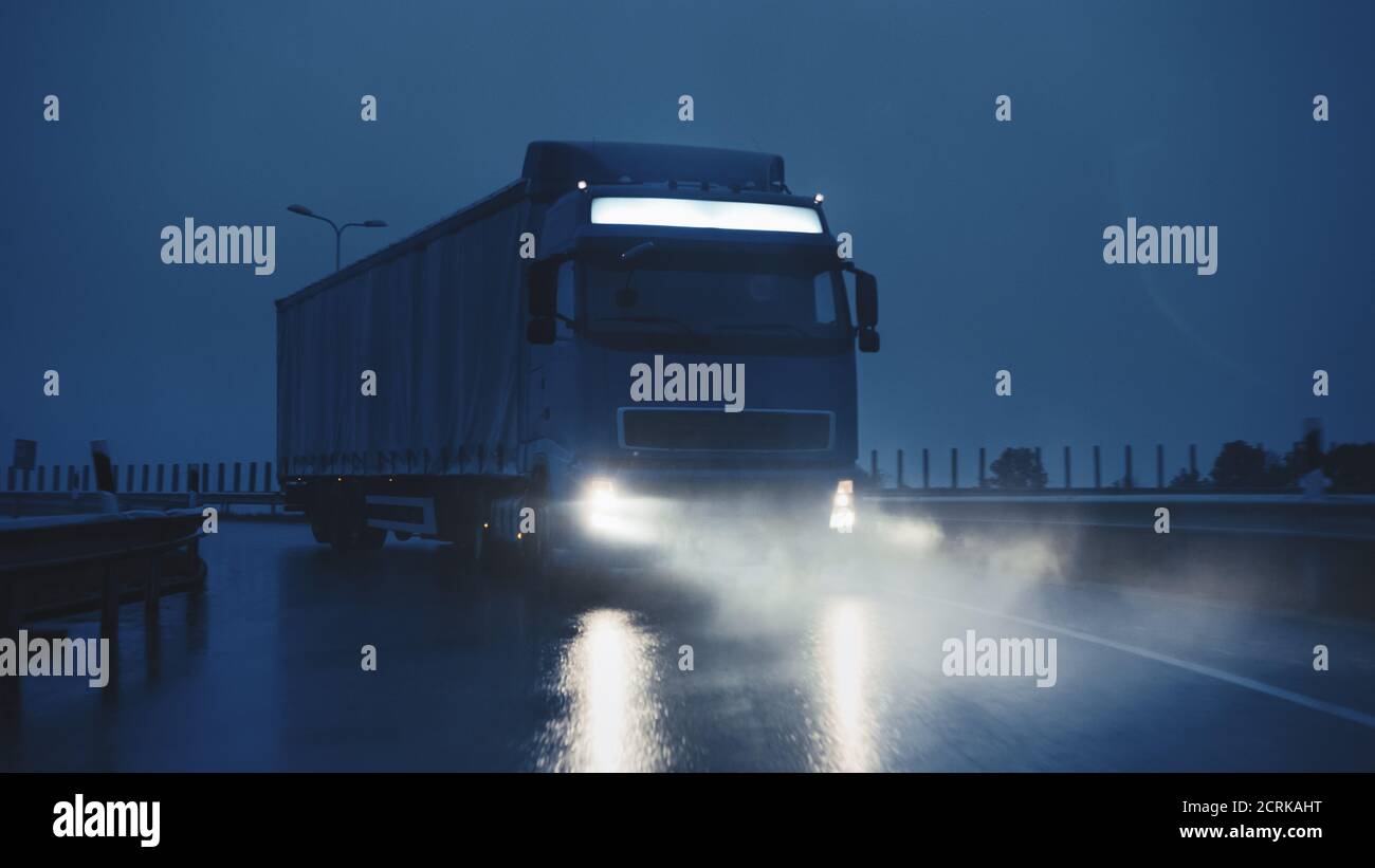 Blue Long Haul semi-Truck con Cargo Trailer Full of Goods viaggia di notte sulla Freeway Road, guidando attraverso il Continente attraverso pioggia, nebbia, neve Foto Stock