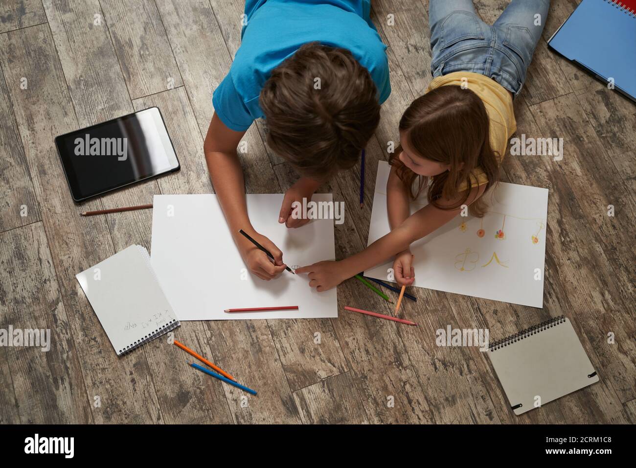 Vista dall'alto del ragazzo caucasico e della ragazza che si stese il pavimento in legno a casa e disegnando su un bianco foglio di carta con matite colorate Foto Stock