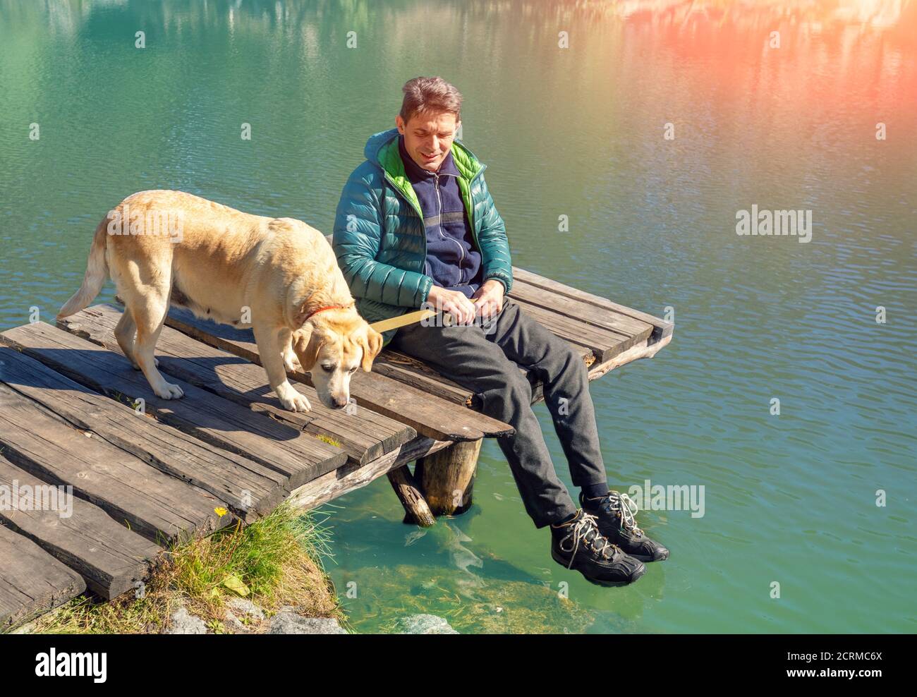 Uomo con il cane Labrador Retriever seduto su un ponte di legno sul lungolago Foto Stock