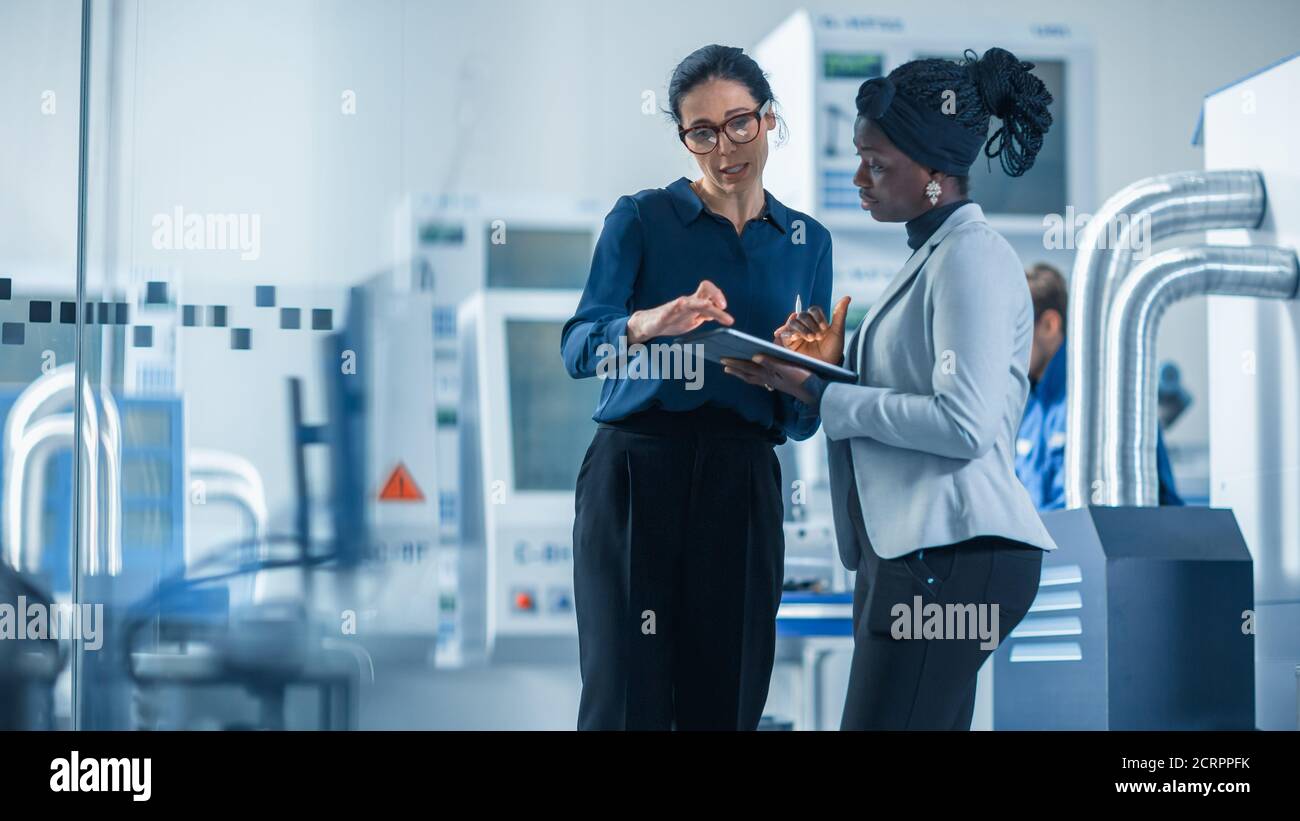 Un ingegnere industriale parla con Project Supervisor, utilizza il computer Tablet digitale e parla della pianificazione moderna della fabbrica. Stabilimento di produzione con Foto Stock