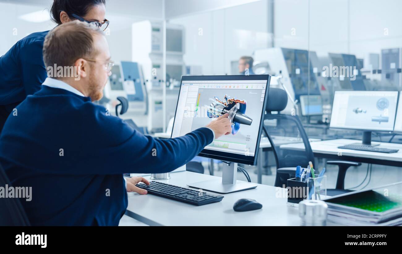 Modern Factory: La Supervisore del progetto femminile parla con un ingegnere industriale maschile che lavora su Personal computer. Utilizzano il software CAD per la progettazione e. Foto Stock