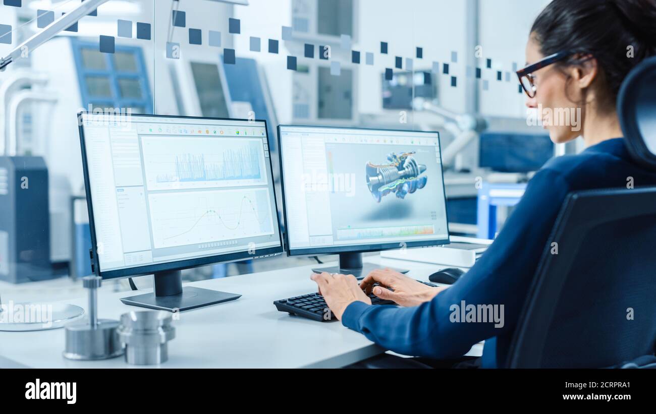 Industrial Female Engineer lavorando su un personal computer, due schermi di monitor mostrano il software CAD con prototipo 3D del nuovo motore ibrido a idrogeno e. Foto Stock