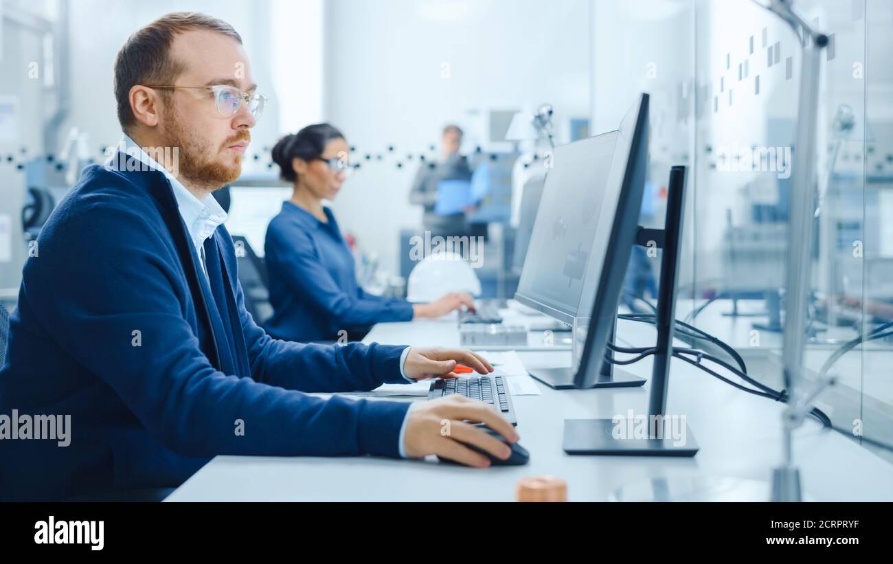 All'interno del team dell'ufficio del vetro della fabbrica degli ingegneri industriali che lavorano su PC, all'esterno dell'armadio nell'officina della struttura moderna lavoratori professionisti che utilizzano Foto Stock