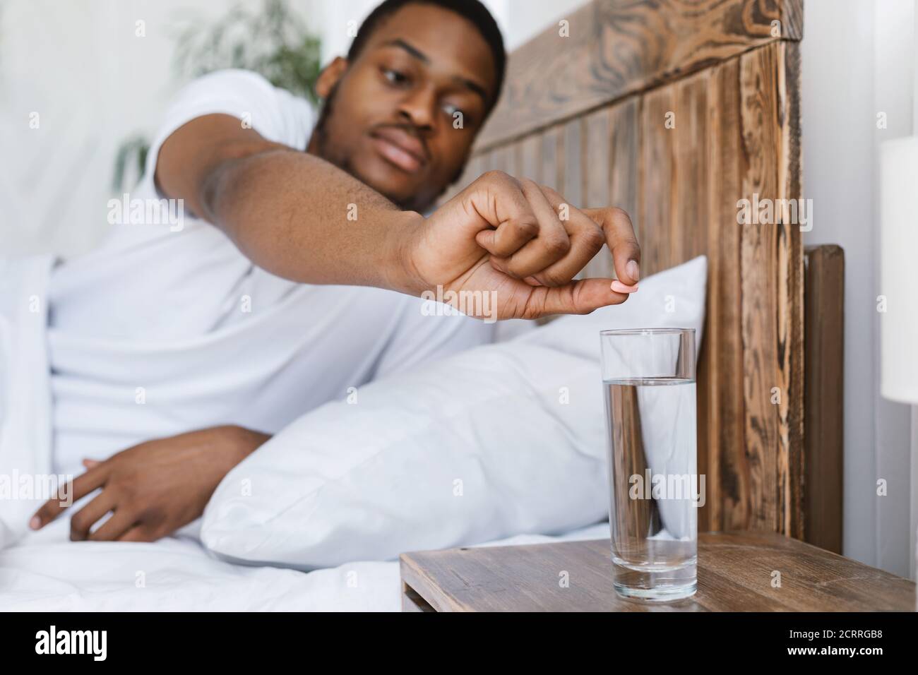 L'uomo africano ammalato che prende la medicina che si trova nel letto a casa Foto Stock