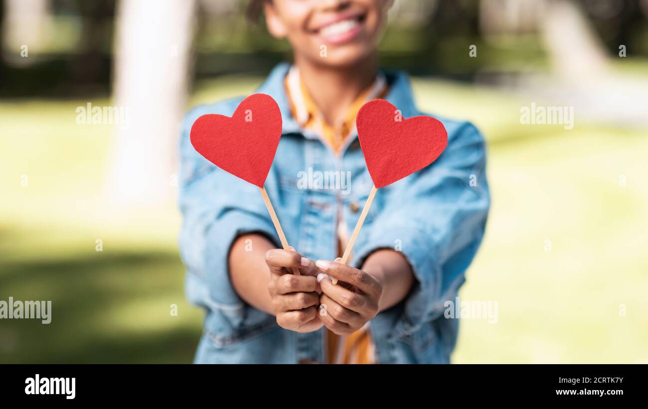 Irriconoscibile donna nera che dà i cuori alla macchina fotografica che si trova in piedi nel parco Foto Stock
