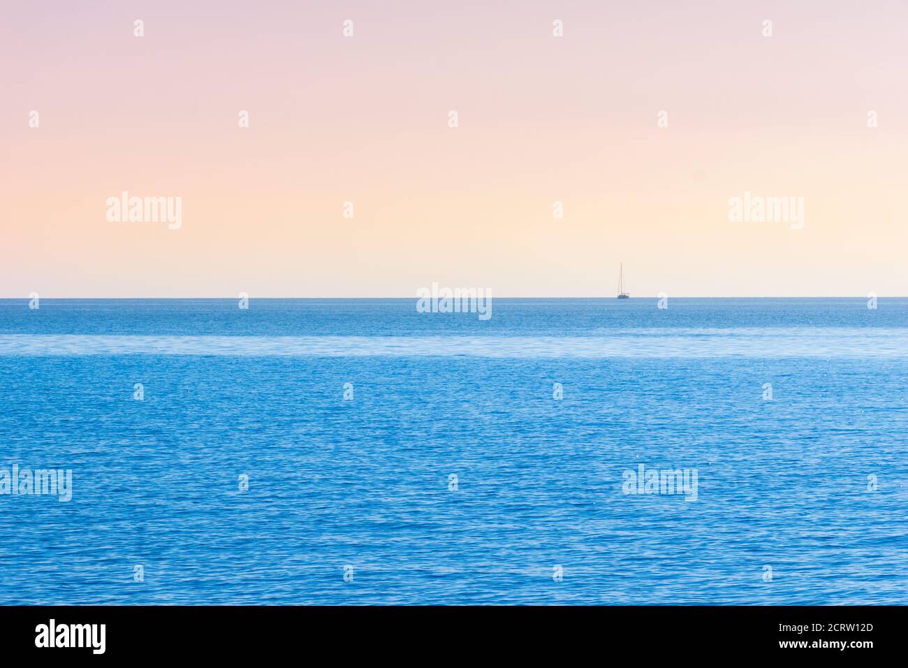 Orizzonte del mare con il cielo rosa pastello e arancione e vela barca in lontananza Foto Stock