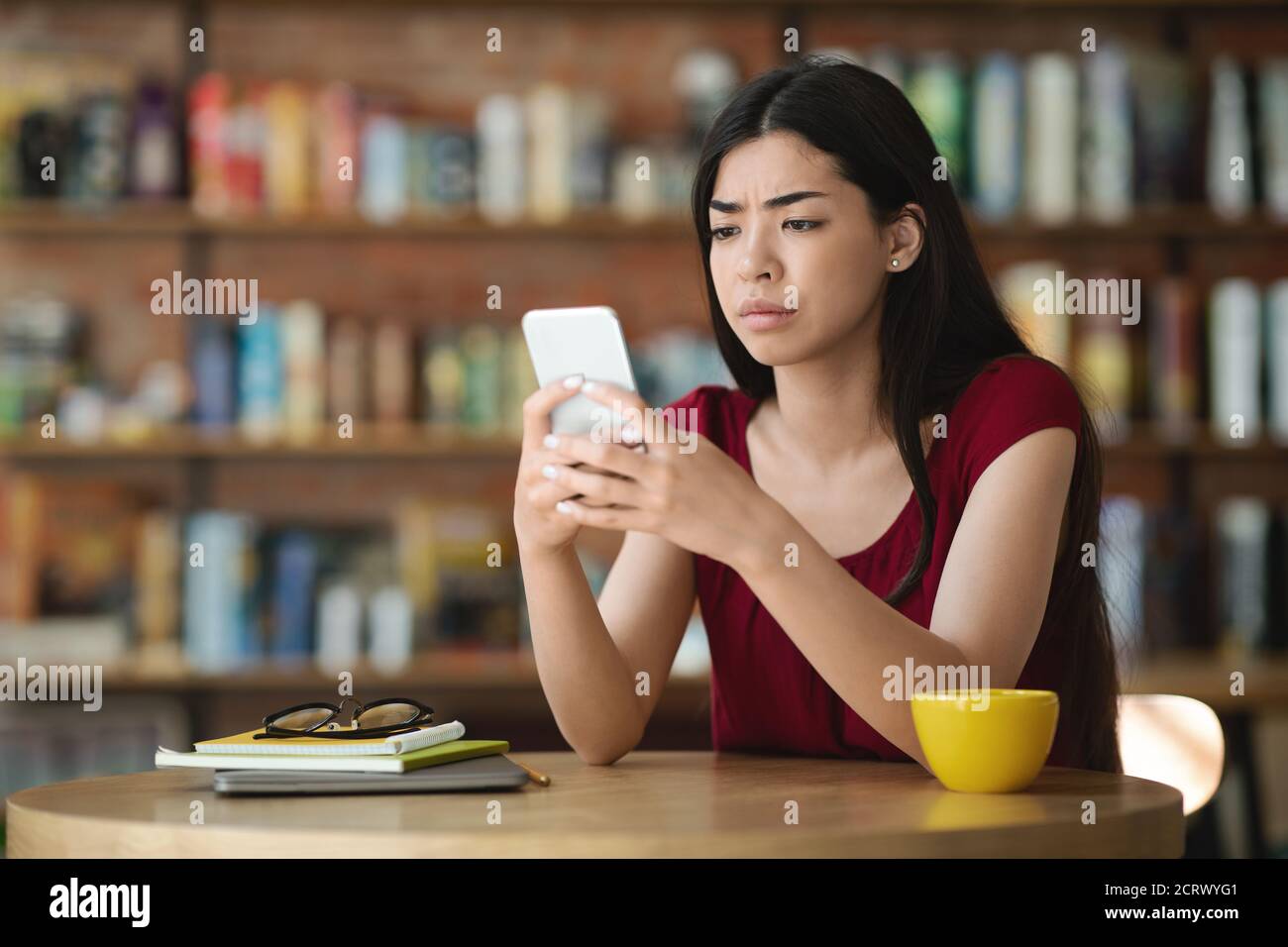 Cattive notizie. Sconvolto Asian Lady guardando lo schermo dello smartphone nel caffè, leggere il messaggio Foto Stock