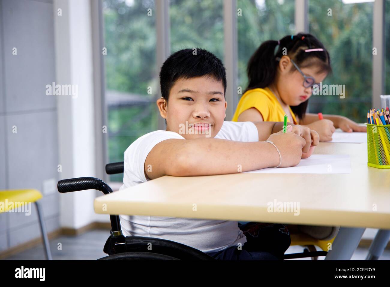 Ragazzo asiatico disabili su sedia a rotelle studia in classe con il suo amico. Foto Stock