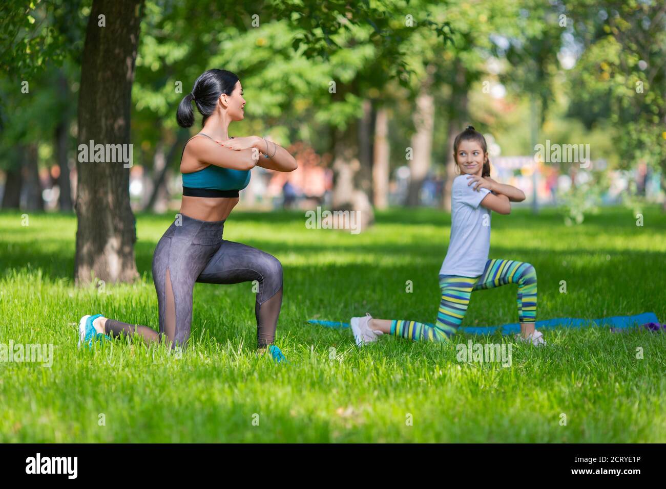 Le ragazze stanno excercising nel parco. Si stanno allungando insieme. Mamma e figlia. Vista laterale. Foto Stock