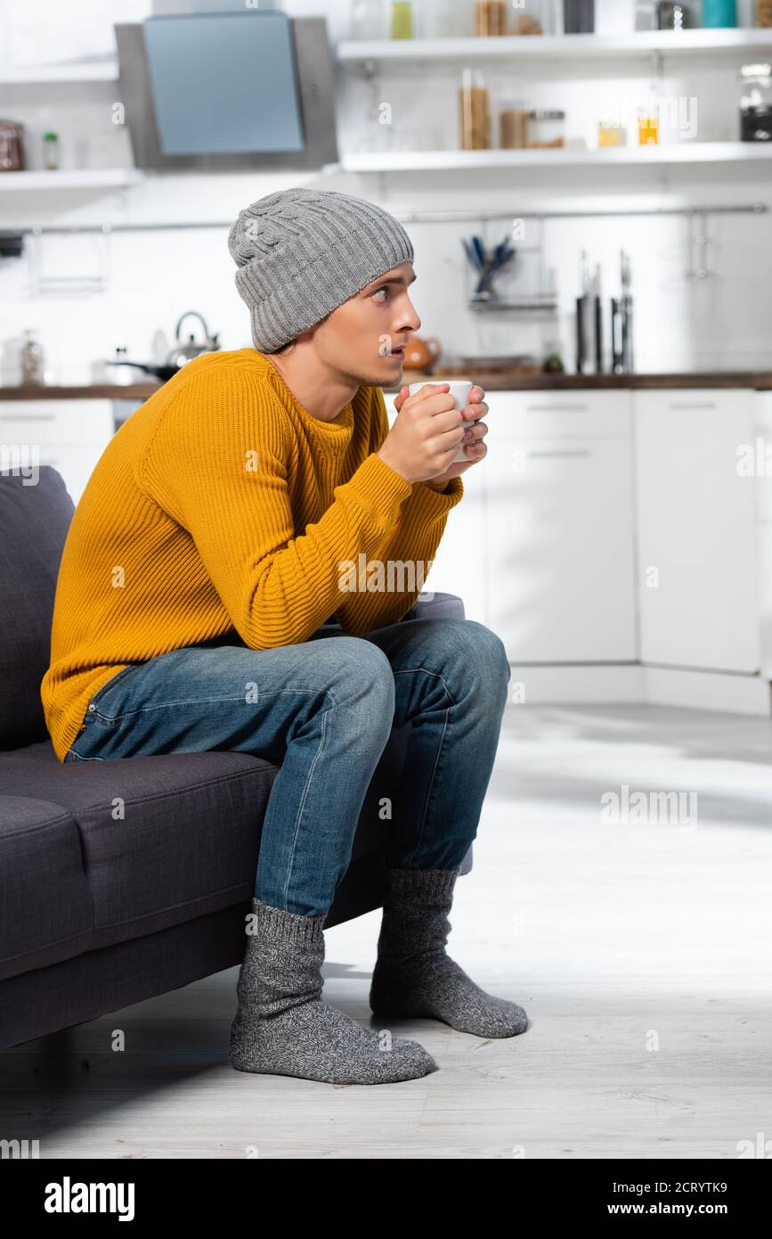 gelare l'uomo in maglia maglione, cappello e calze che tengono una tazza di  bevanda calda in cucina Foto stock - Alamy