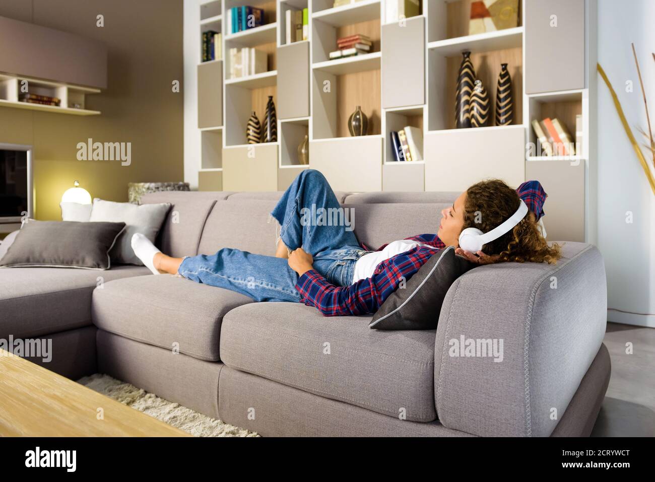 Giovane donna che si rilassa nel soggiorno o nel salotto a casa su un divano per ascoltare la musica con le cuffie stereo Foto Stock