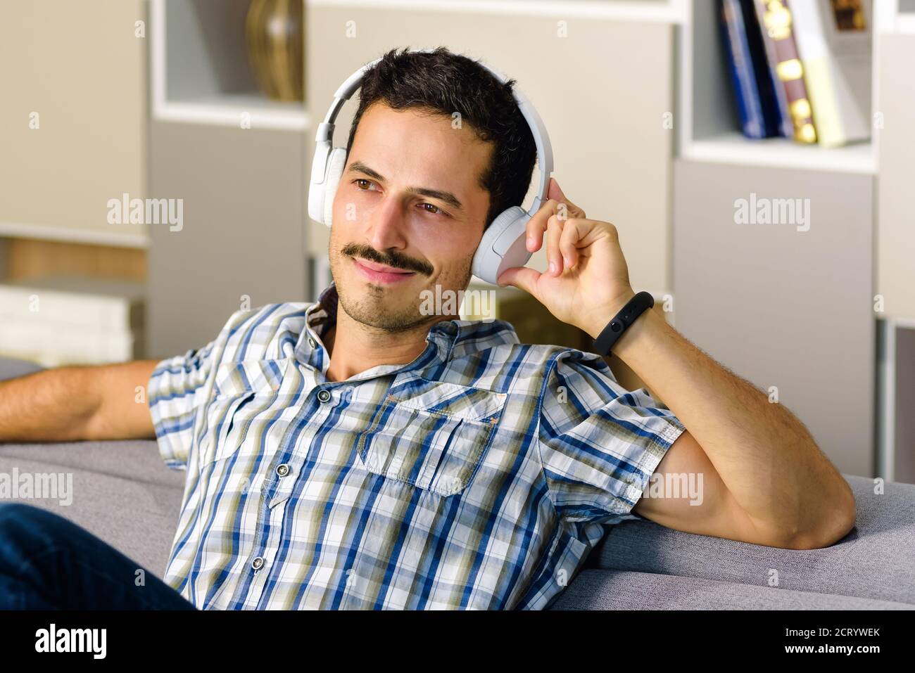 Uomo rilassante ascoltando la musica sulle cuffie stereo di un comodo divano a casa sorridente con piacere in un concetto di intrattenimento personale Foto Stock