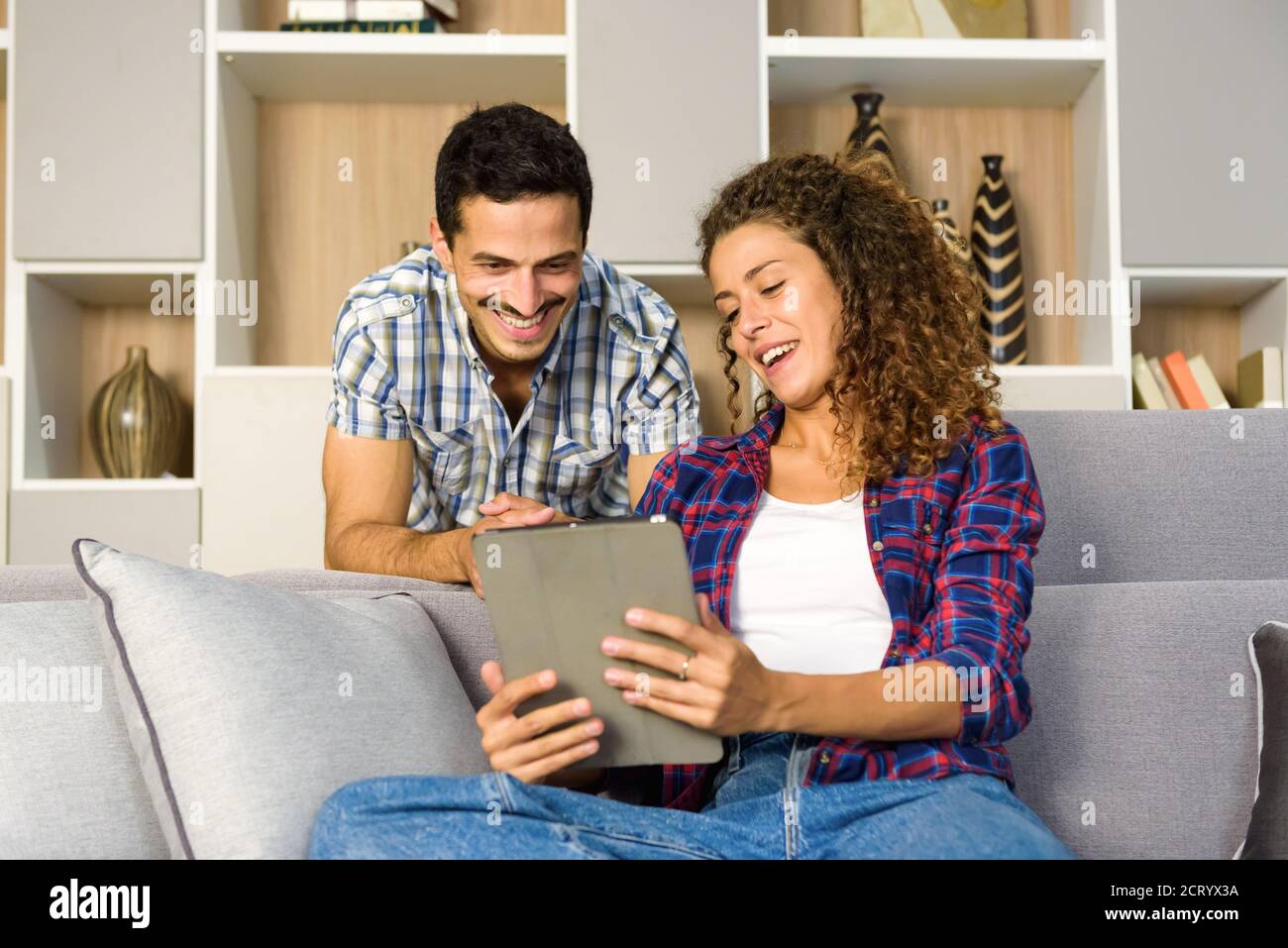Felice giovane coppia che guarda i media su un tablet insieme il soggiorno a casa sorridendo con piacere e piacere Foto Stock
