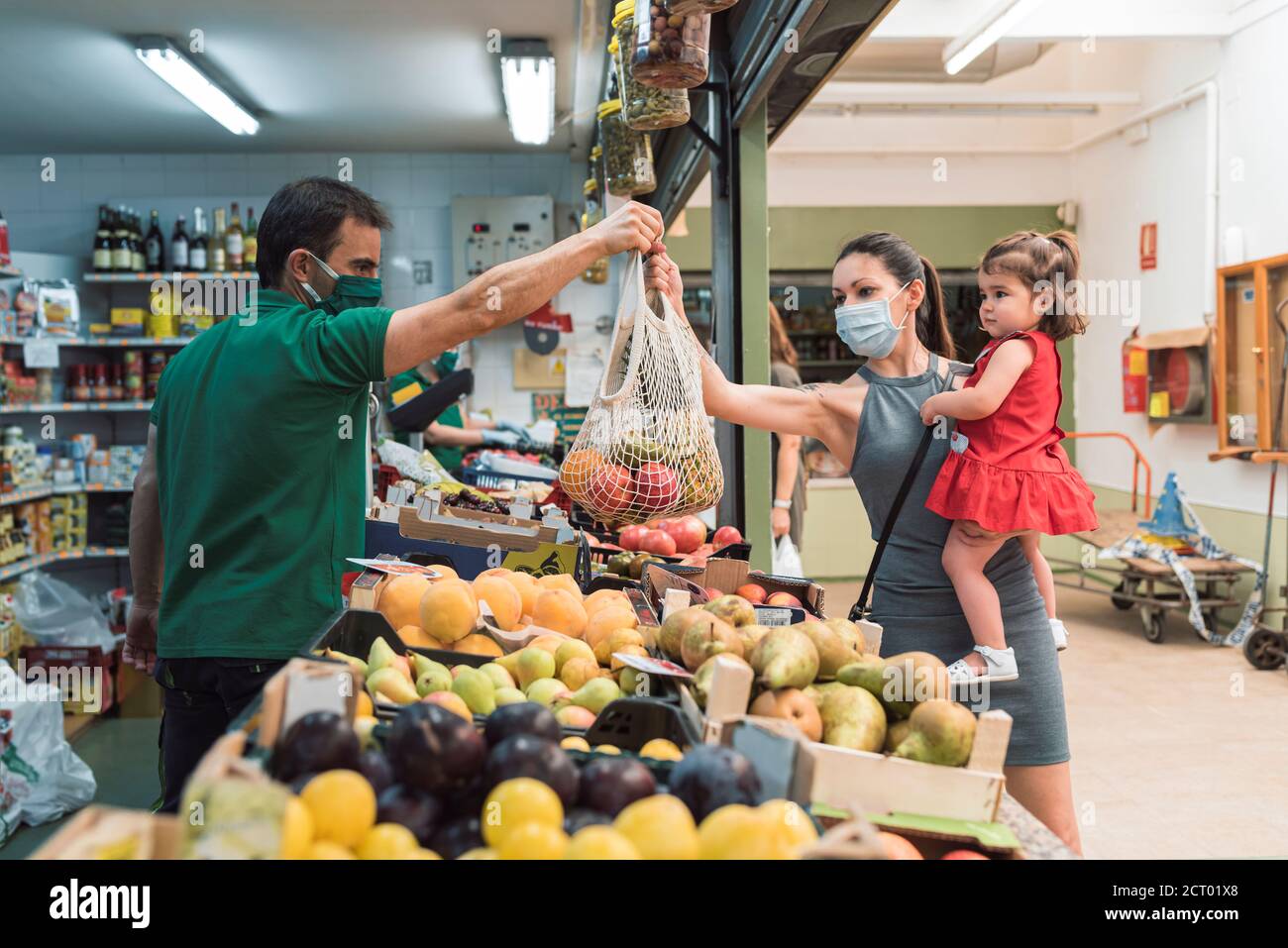 Una giovane donna con una maschera che acquista presso il negozio di frutta con sua figlia. Concetto di shopping Foto Stock