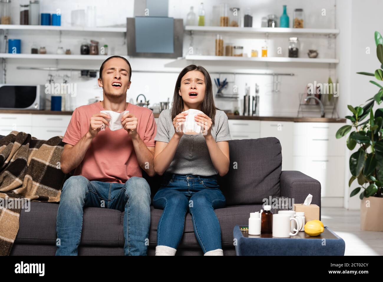 ammalare la coppia starnutire mentre si siede in cucina con tazze di bevanda calda Foto Stock